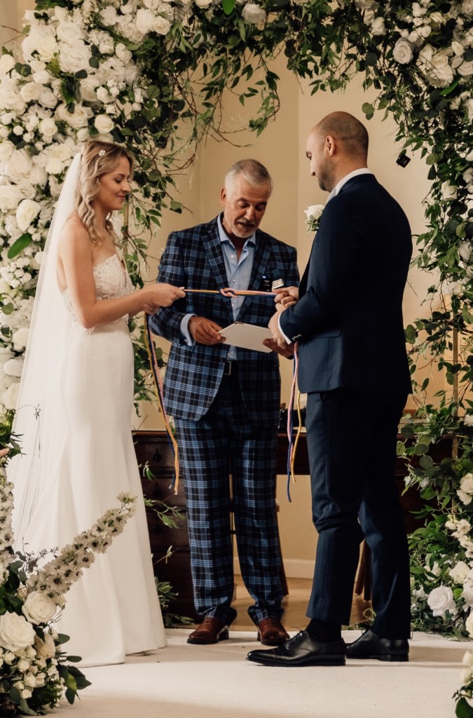 Wedding Celebrant performing handfasting symbolic action during Wedding at Farnham Castle, Surrey